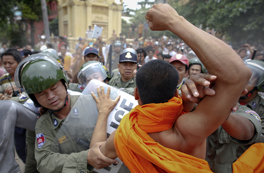 Riot policemen protect a man as a monk tries to punch him after an incident at a polling station in Phnom Penh