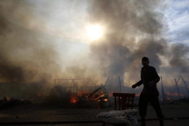 A migrant is seen in silhouette as smoke fills the sky from burning makeshift shelters in the "Jungle" on the third day of their evacuation and transfer to reception centers in France, as part of the dismantlement of the camp in Calais