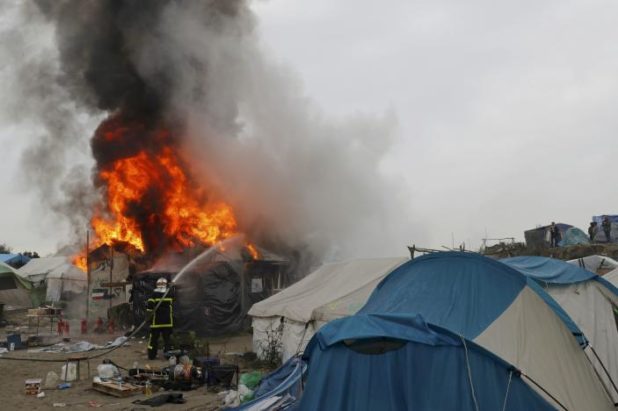 Firefighters extinguish burning makeshift shelters and tents in the "Jungle" on the third day of the evacuation of migrants and their transfer to reception centers in France, as part of the dismantlement of the camp in Calais