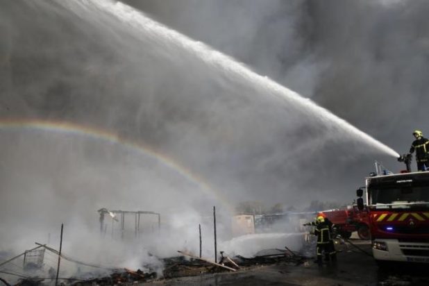 A rainbow is seen as firmen work to extinguish burning makeshift shelters in the "Jungle" on the third day of the evacuation and transfer of migrants to reception centers in France, as part of the dismantlement of the camp in Calais