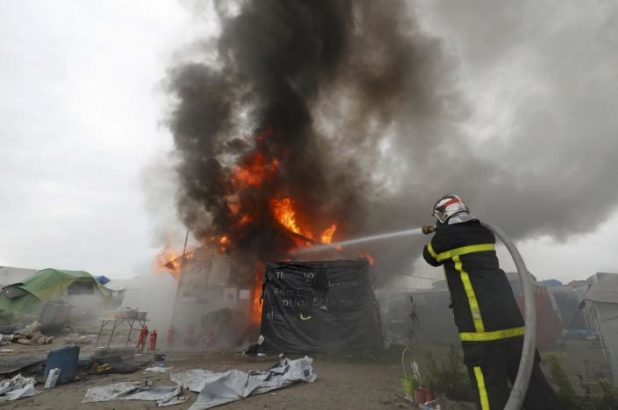 Firefighters extinguish burning makeshift shelters and tents in the "Jungle" on the third day of the evacuation of migrants and their transfer to reception centers in France, as part of the dismantlement of the camp in Calais