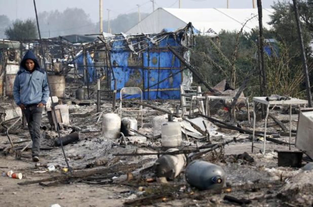 A migrant walks past the charred debris from makeshift shelters and tents in the "Jungle" on the third day of their evacuation, as part of the dismantlement of the camp in Calais
