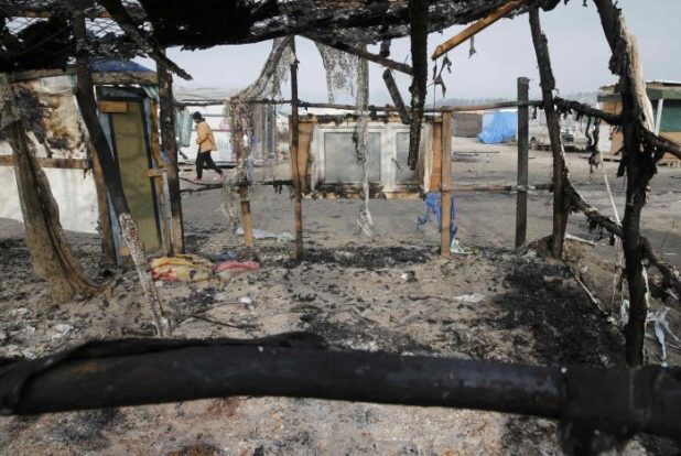 A migrant walks past charred debris from makeshift shelters and tents in the "Jungle" on the third day of their evacuation, as part of the dismantlement of the camp in Calais