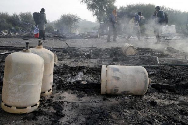 Migrants carry their belongings as they walk past the charred debris from makeshift shelters and tents in the "Jungle" on the third day of their evacuation, as part of the dismantlement of the camp in Calais
