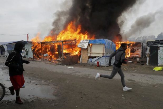 Migrants run past a burning makeshift shelters in the "Jungle" on the third day of their evacuation, as part of the dismantlement of the camp in Calais