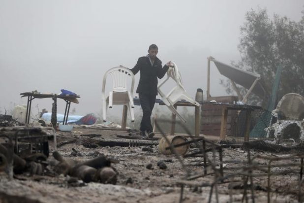 A migrant carries chairs as he walks through the charred debris from makeshift shelters and tents in the "Jungle" on the third day of their evacuation and transfer to reception centers in France, as part of the dismantlement of the camp in Calais