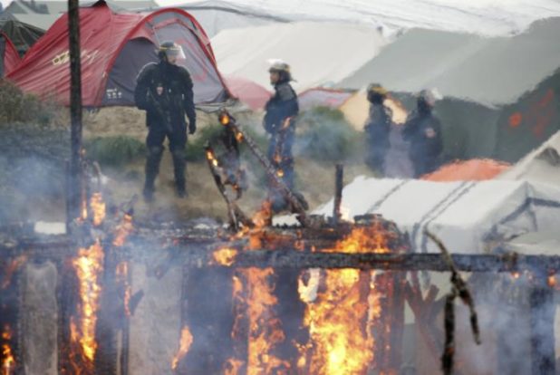 French CRS riot police secure the area near burning makeshift shelters and tents in the "Jungle" on the third day of the evacuation of migrants, as part of the dismantlement of the camp in Calais