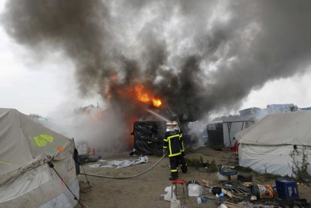 Firefighters extinguish burning makeshift shelters and tents in the "Jungle" on the third day of the evacuation of migrants and their transfer to reception centers in France, as part of the dismantlement of the camp in Calais