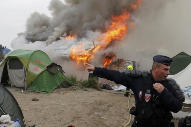 French CRS riot police secure the area near burning makeshift shelters and tents in the "Jungle" on the third day of the evacuation of migrants and their transfer to reception centers in France, as part of the dismantlement of the camp in Calais